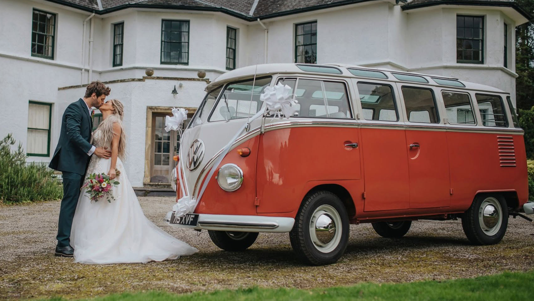 Bride and groom kissing in front of red and white 1962 Volkswagen Split Screen Microbus.
