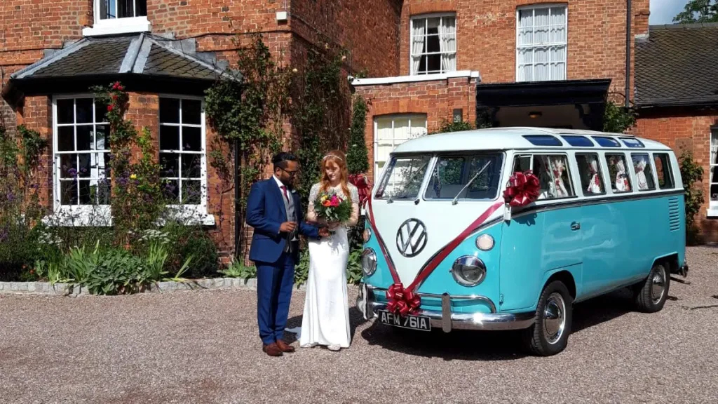 Bride and groom beside blue and white Volkswagen Split Screen Samba campervan outside Wrexham wedding venue.