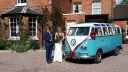 Bride and groom beside blue and white Volkswagen Split Screen Samba campervan outside Wrexham wedding venue.