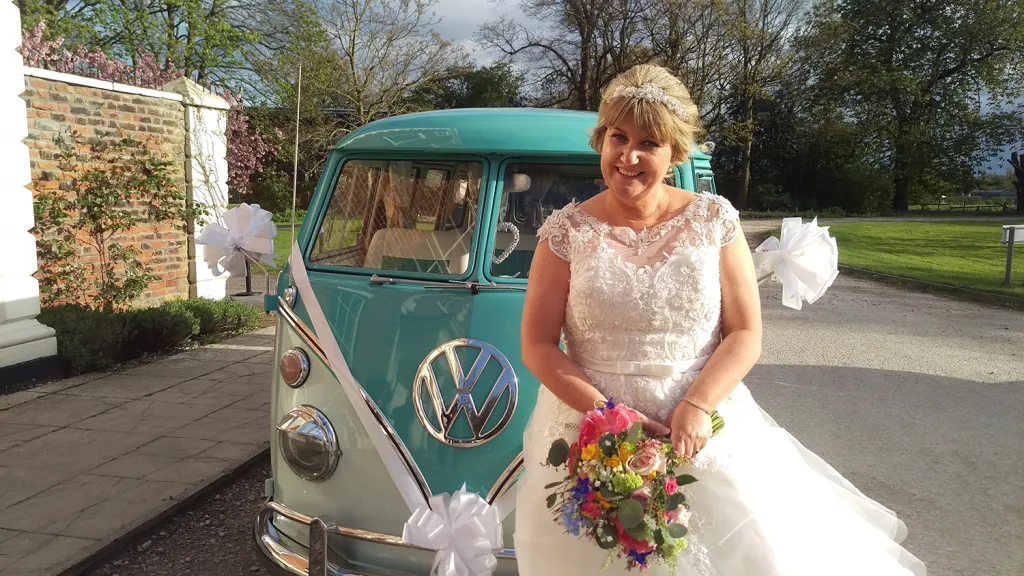 Bride standing in front of turquoise and white 1967 Volkswagen Split Screen campervan decorated for a wedding.