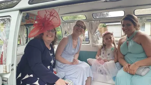 Bridesmaids seated inside blue and white Volkswagen Split Screen Samba campervan with spacious interior.