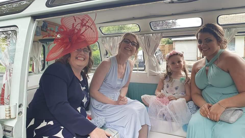 Bridesmaids seated inside blue and white Volkswagen Split Screen Samba campervan with spacious interior.