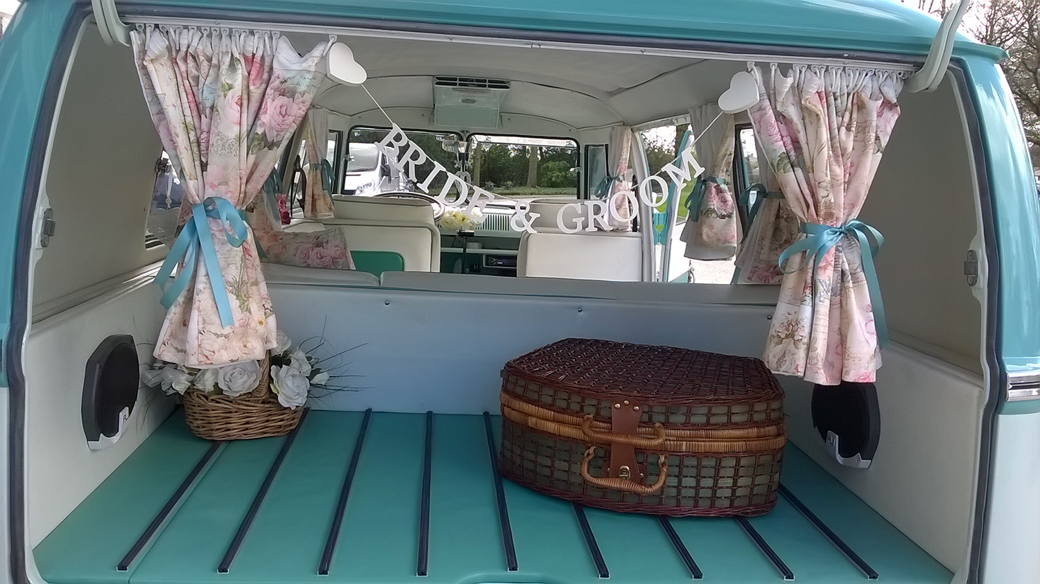 Rear interior of turquoise and white Volkswagen Split Screen campervan viewed through open rear doors.