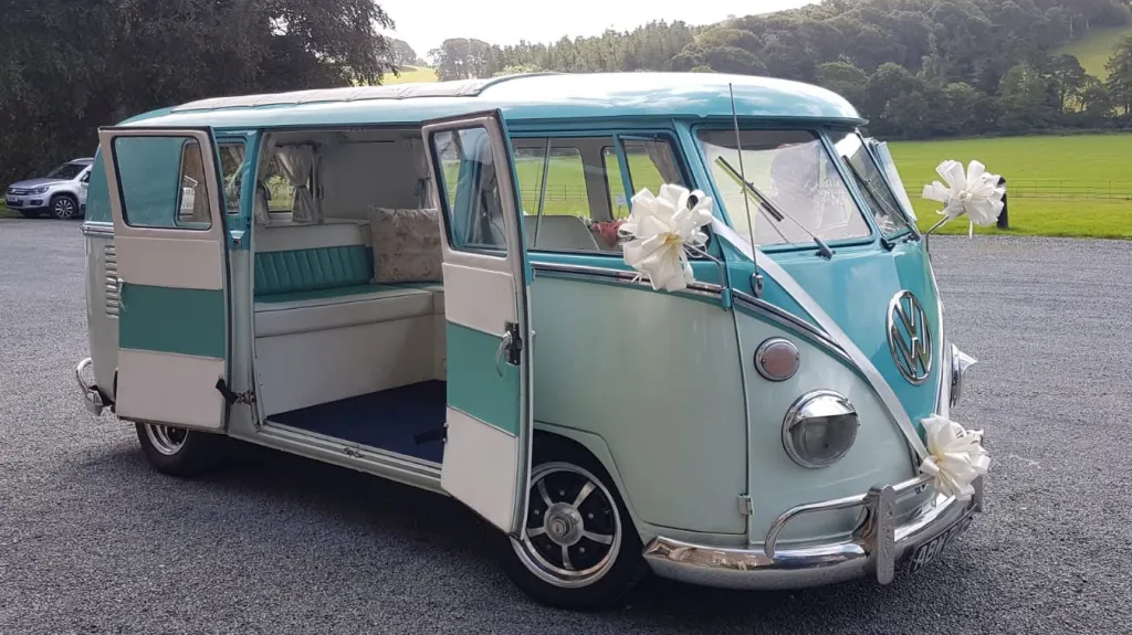 Turquoise and white 1967 Volkswagen Split Screen campervan with side door open parked outside wedding venue in Denbighshire.