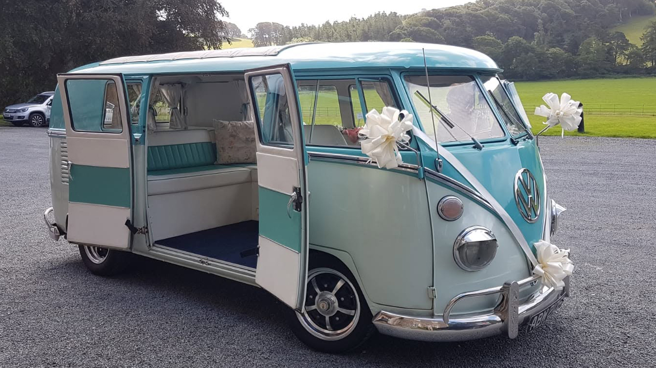 Turquoise and white 1967 Volkswagen Split Screen campervan with side door open parked outside wedding venue in Denbighshire.