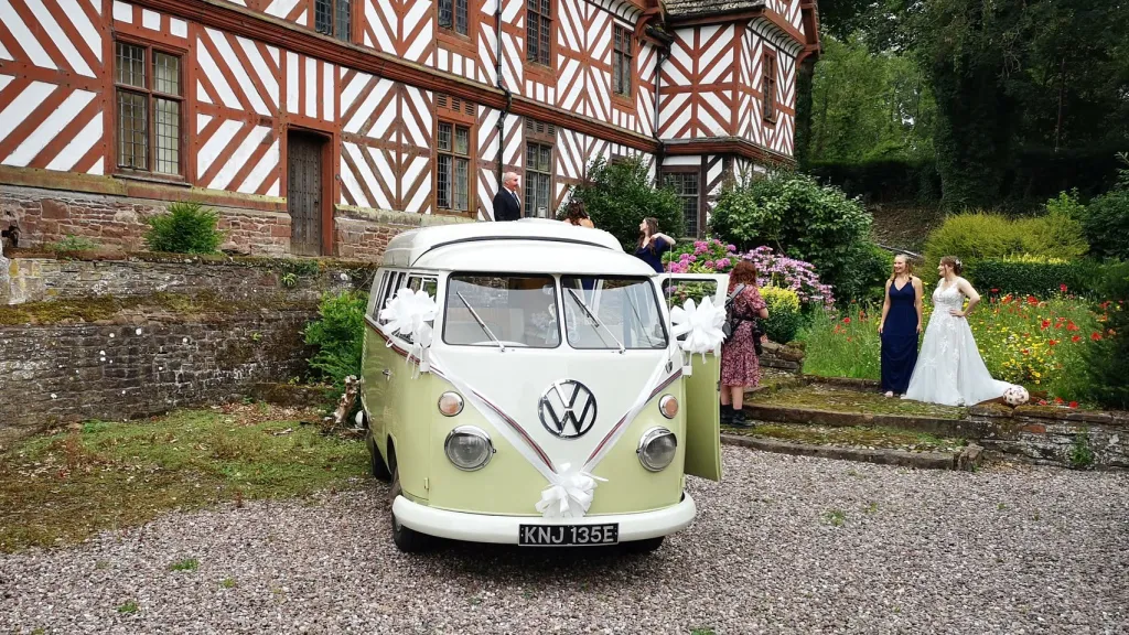 Cream and green Volkswagen Split Screen campervan parked outside traditional countryside wedding venue.