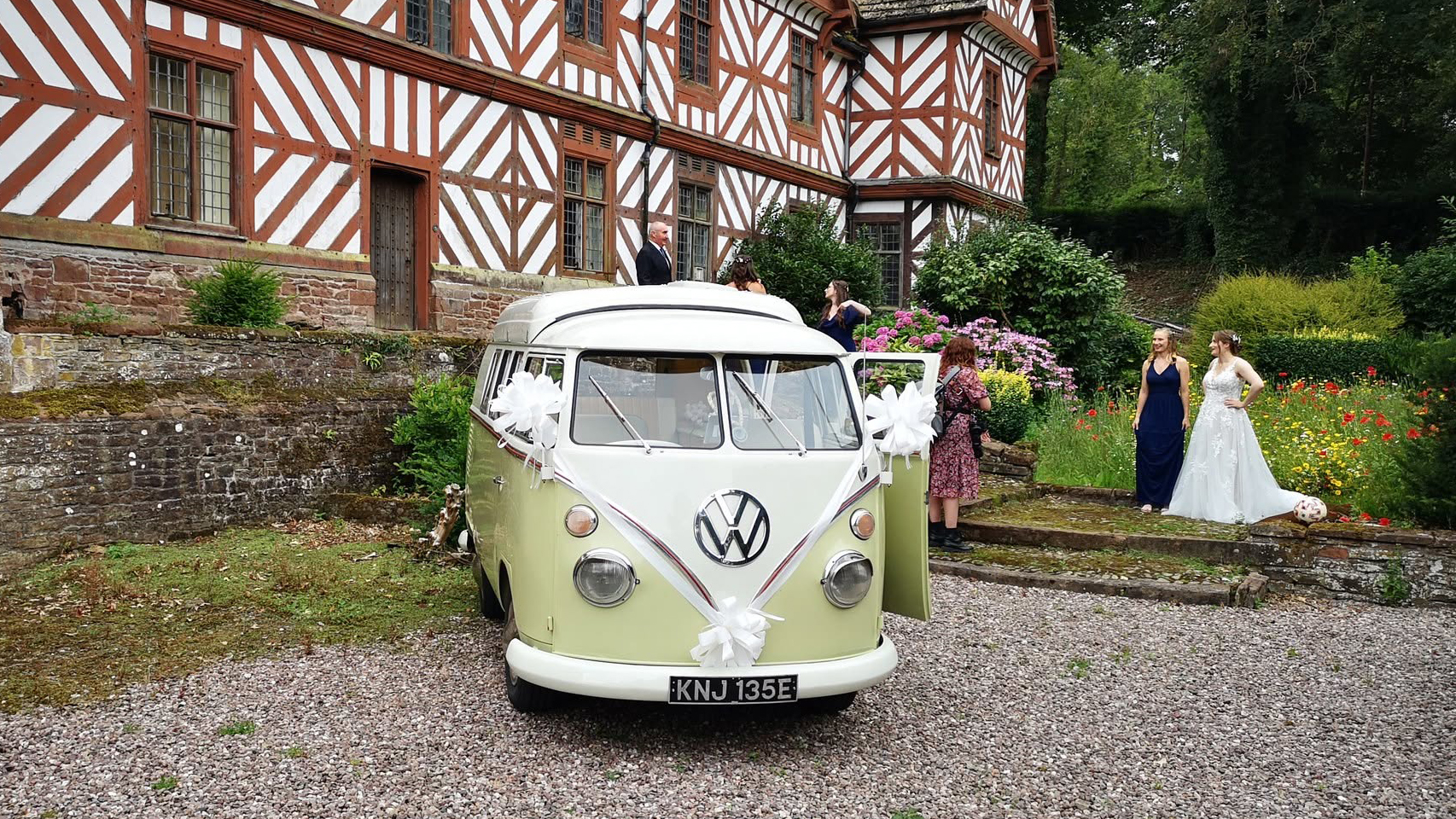Cream and green Volkswagen Split Screen campervan parked outside traditional countryside wedding venue.