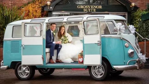 Bride and groom seated inside turquoise and white Volkswagen Split Screen campervan with side door open.