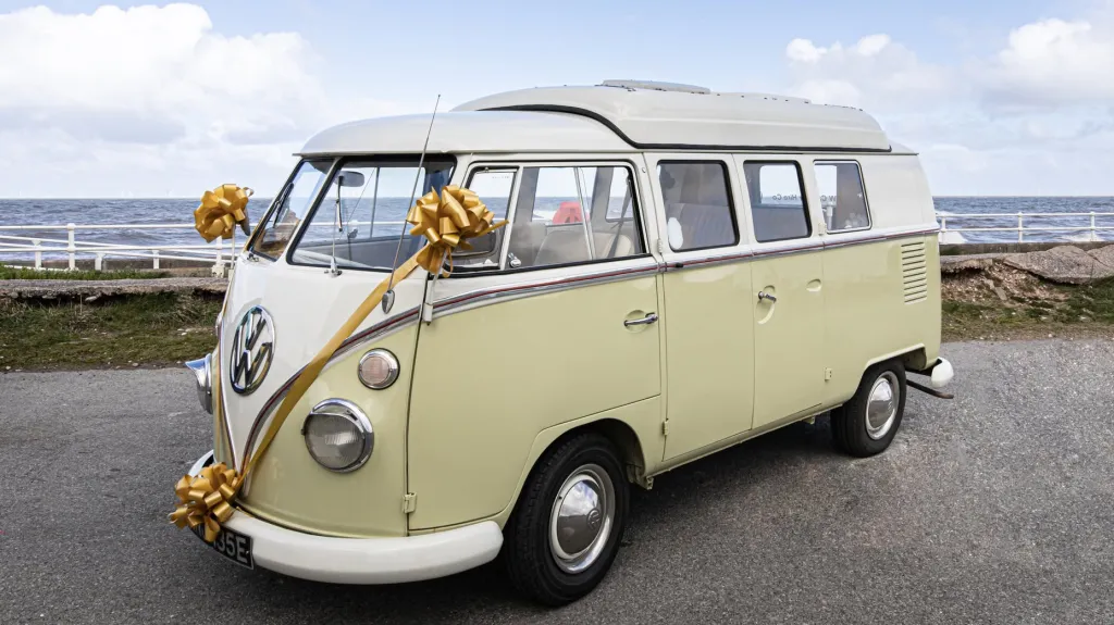 Cream and green Volkswagen Split Screen campervan decorated with wedding ribbons beside the coast in North Wales.