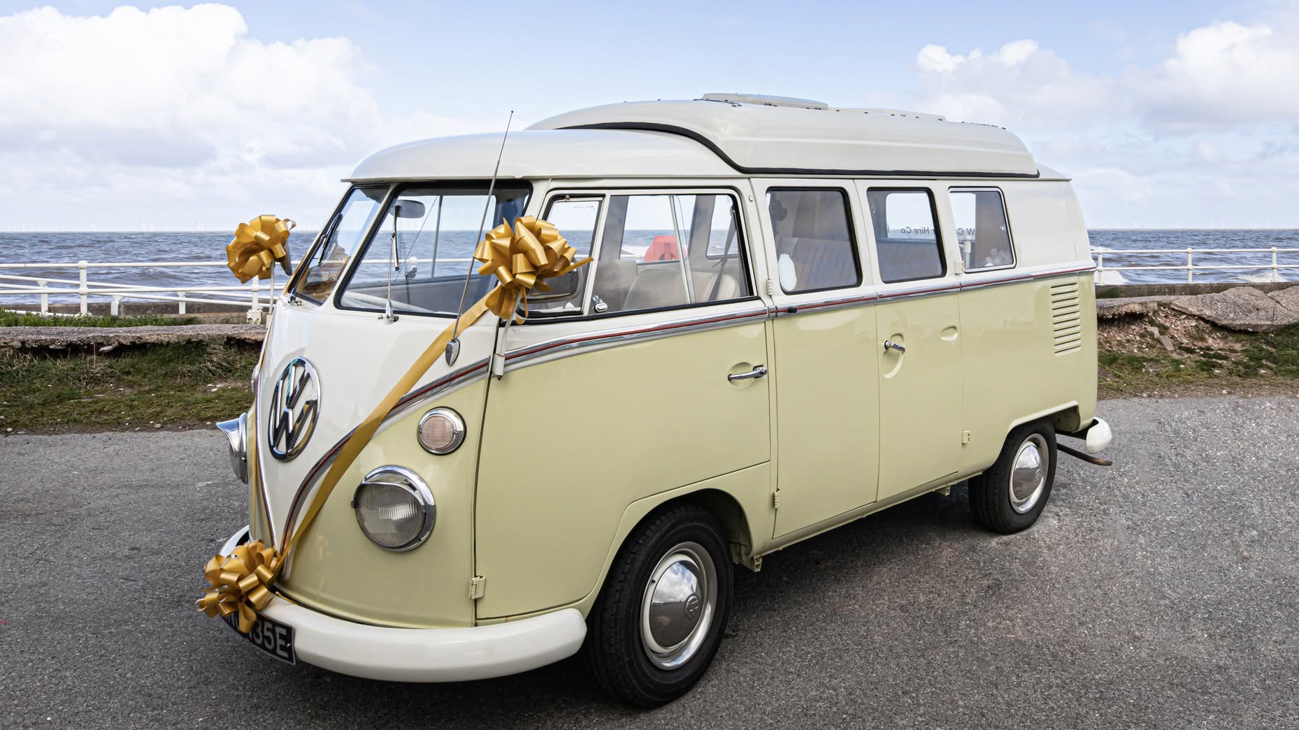 Cream and green Volkswagen Split Screen campervan decorated with wedding ribbons beside the coast in North Wales.