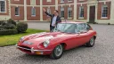 Front left view of red 1969 Jaguar E Type with chrome wire wheels outside historic manor house.