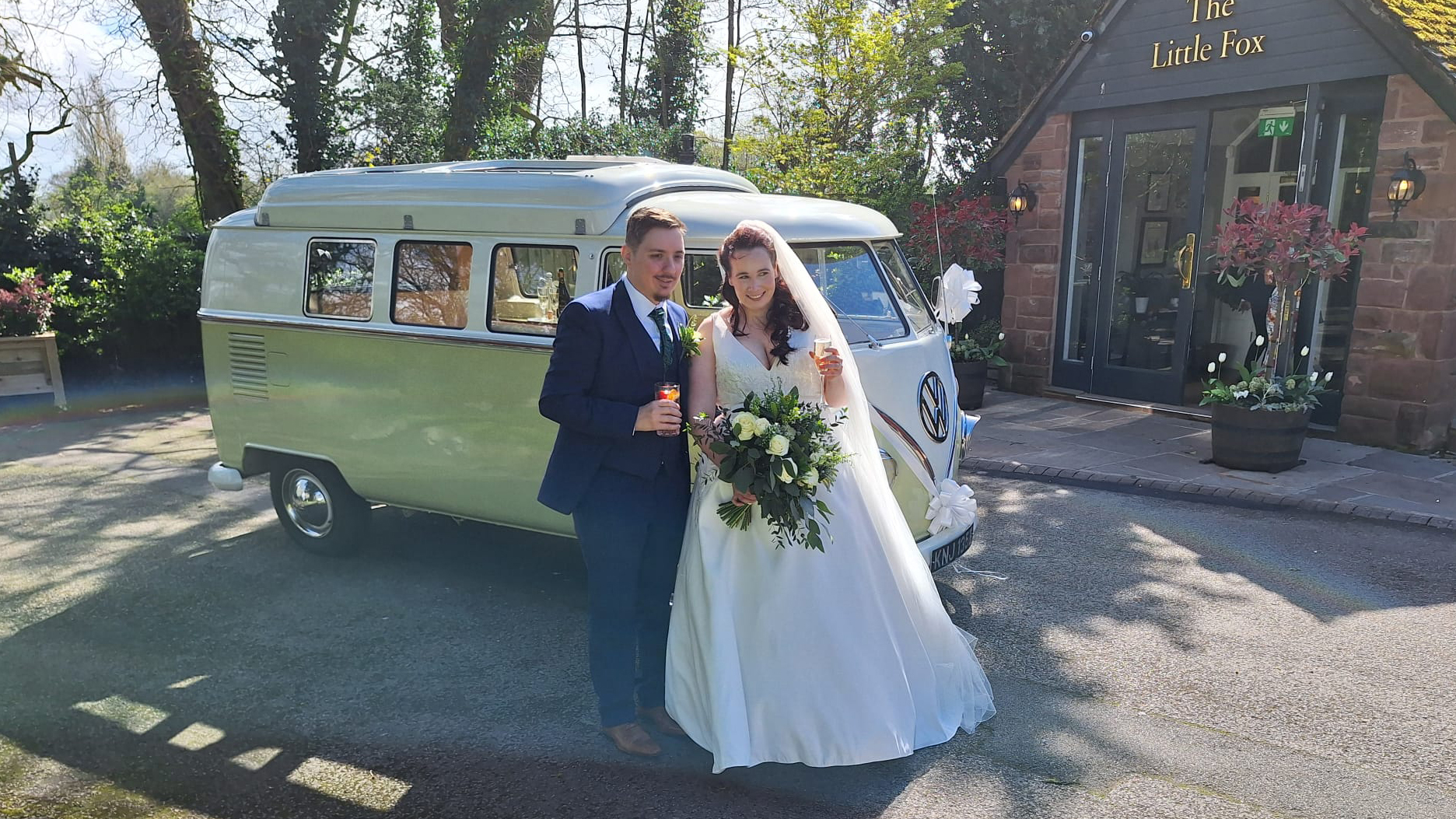 Bride and groom standing beside cream and green Volkswagen Split Screen campervan outside wedding venue.