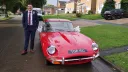 Groom standing beside red 1969 Jaguar E Type decorated with wedding ribbons.