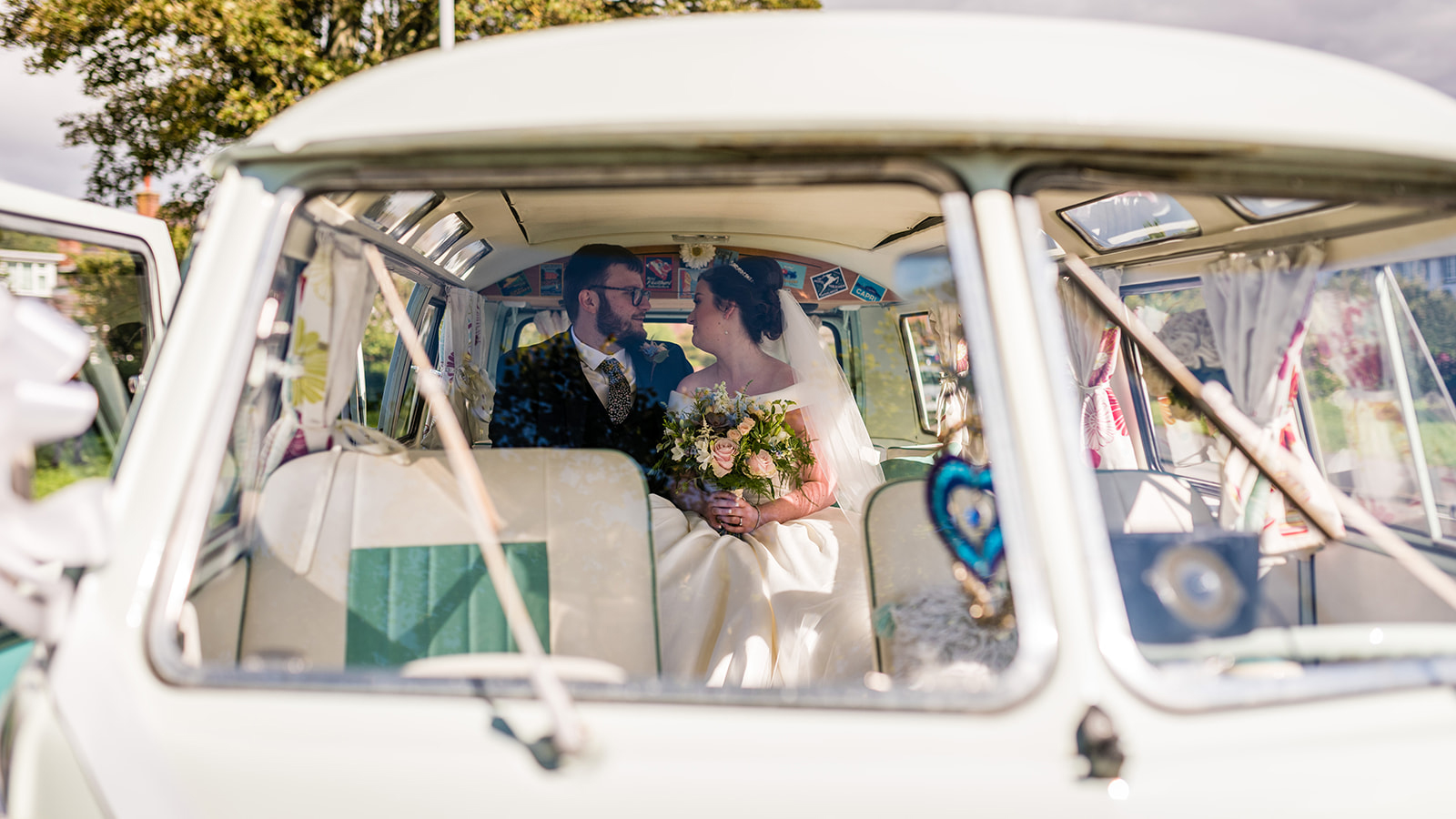 Bride and groom sharing a kiss inside blue and white Volkswagen Split Screen Samba campervan.