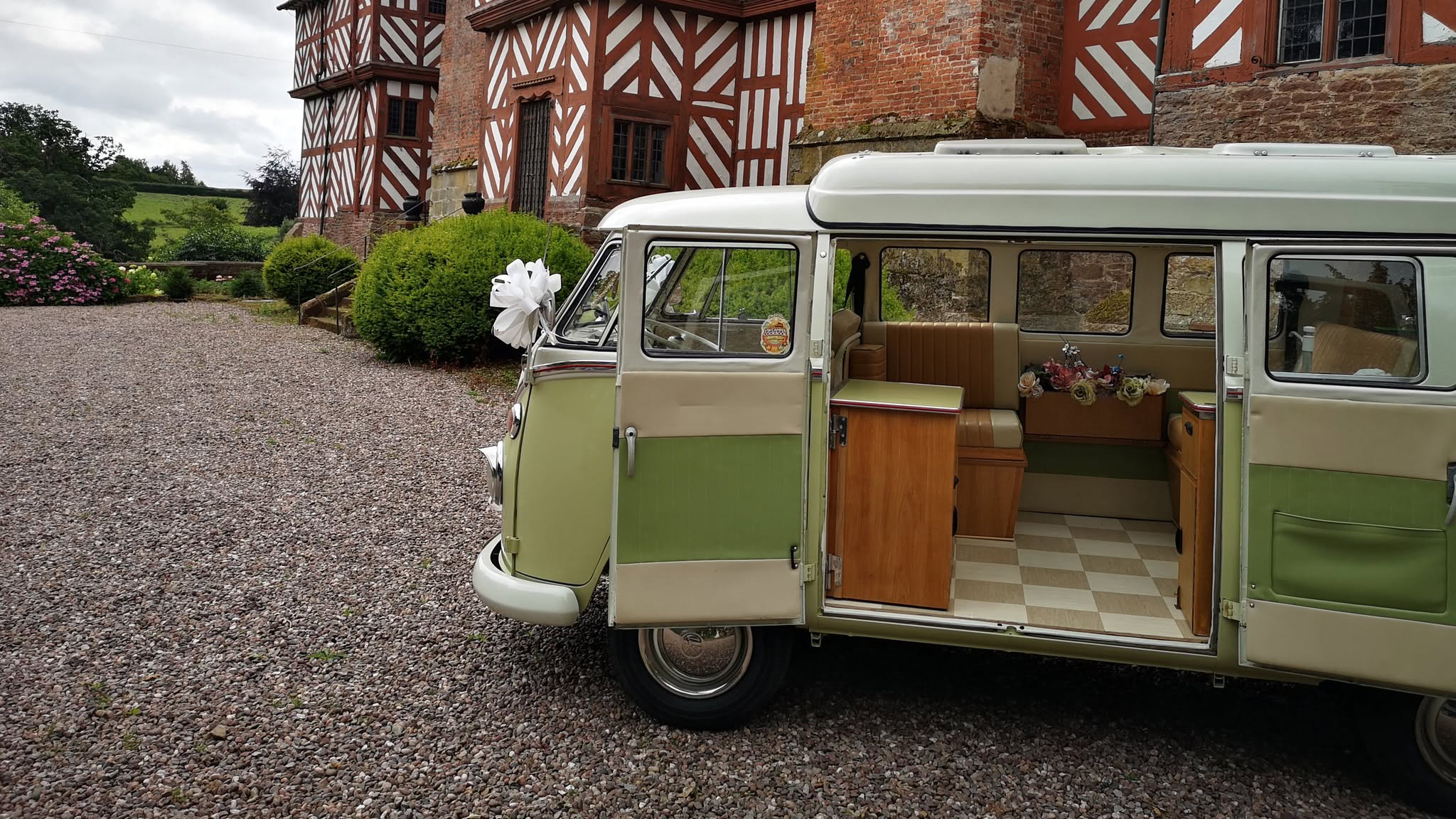 Side view of cream and green Volkswagen Split Screen campervan with rear side door open showing the interior.