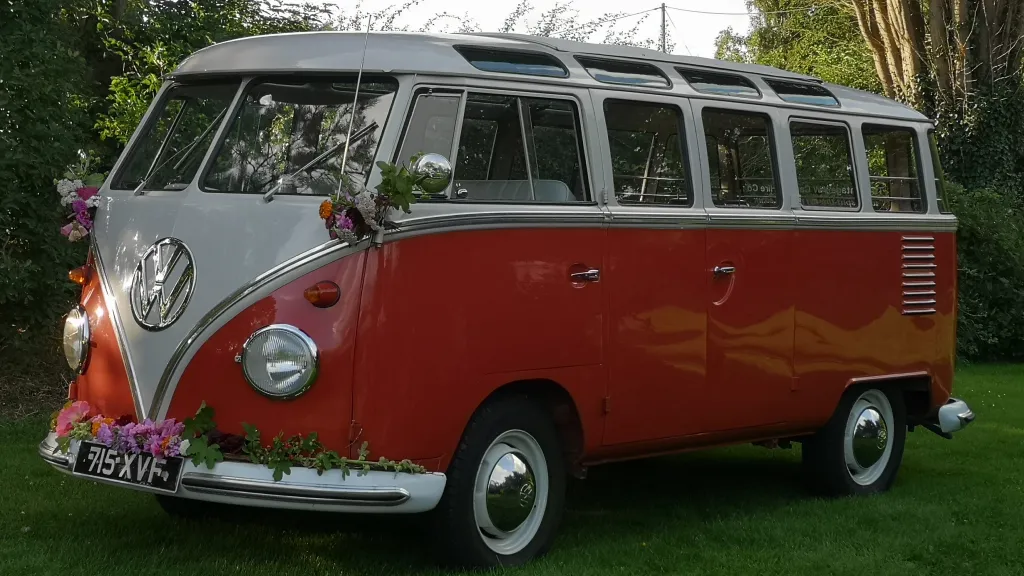 Left side view of red and white Volkswagen Split Screen 23 Window Microbus with chrome bumpers and safari roof windows.