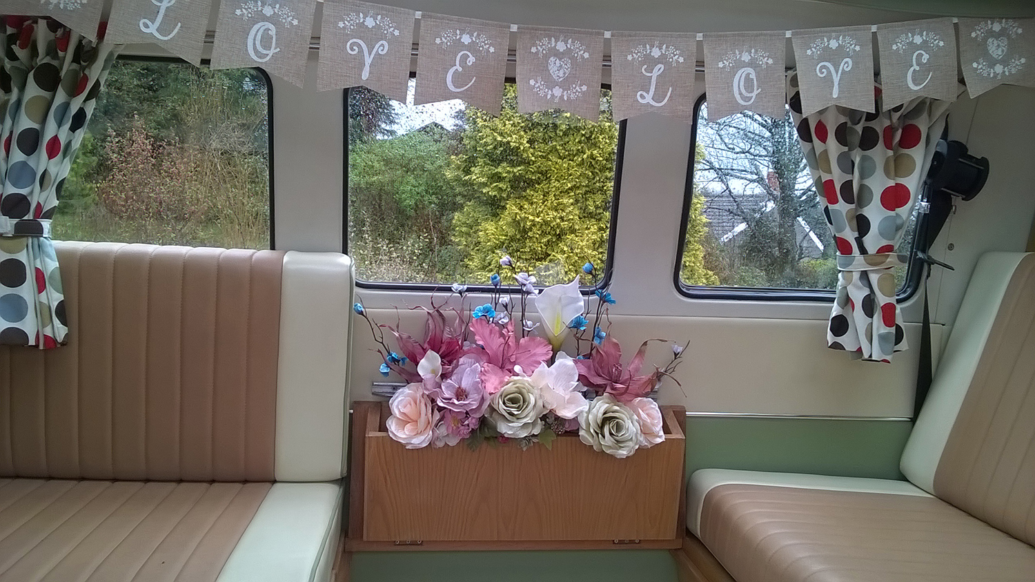 Rear seating area inside cream and green Volkswagen Split Screen campervan with floral decorations.