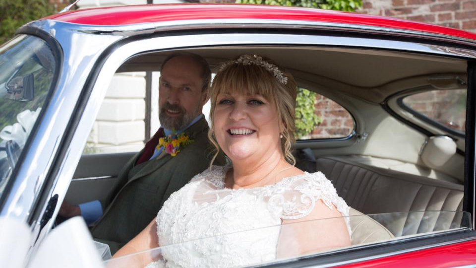 Bride smiling inside red 1969 Jaguar E Type showing the cream interior and classic cabin.