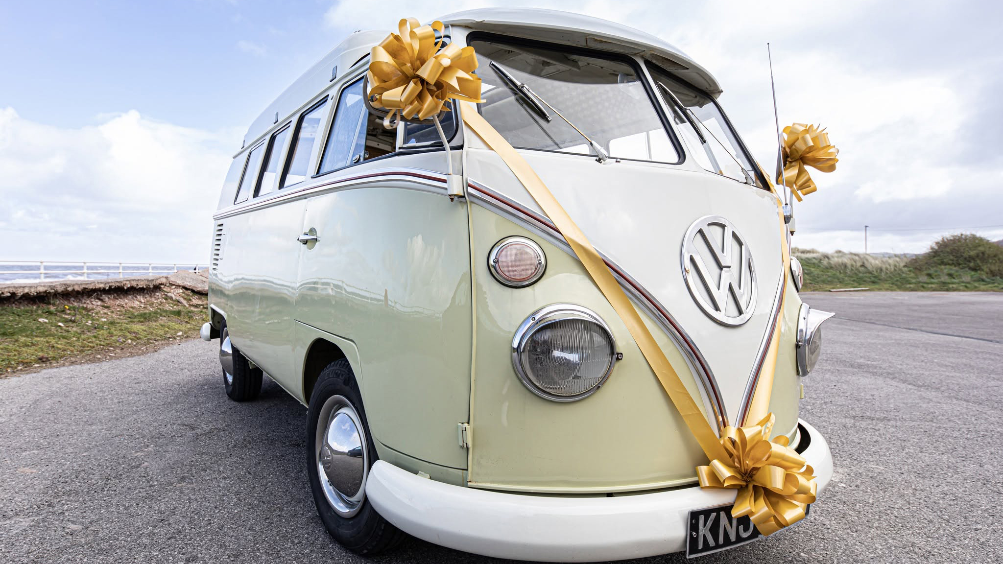 Front three quarter view of cream and green Volkswagen Split Screen campervan decorated with wedding ribbons in Wrexham.