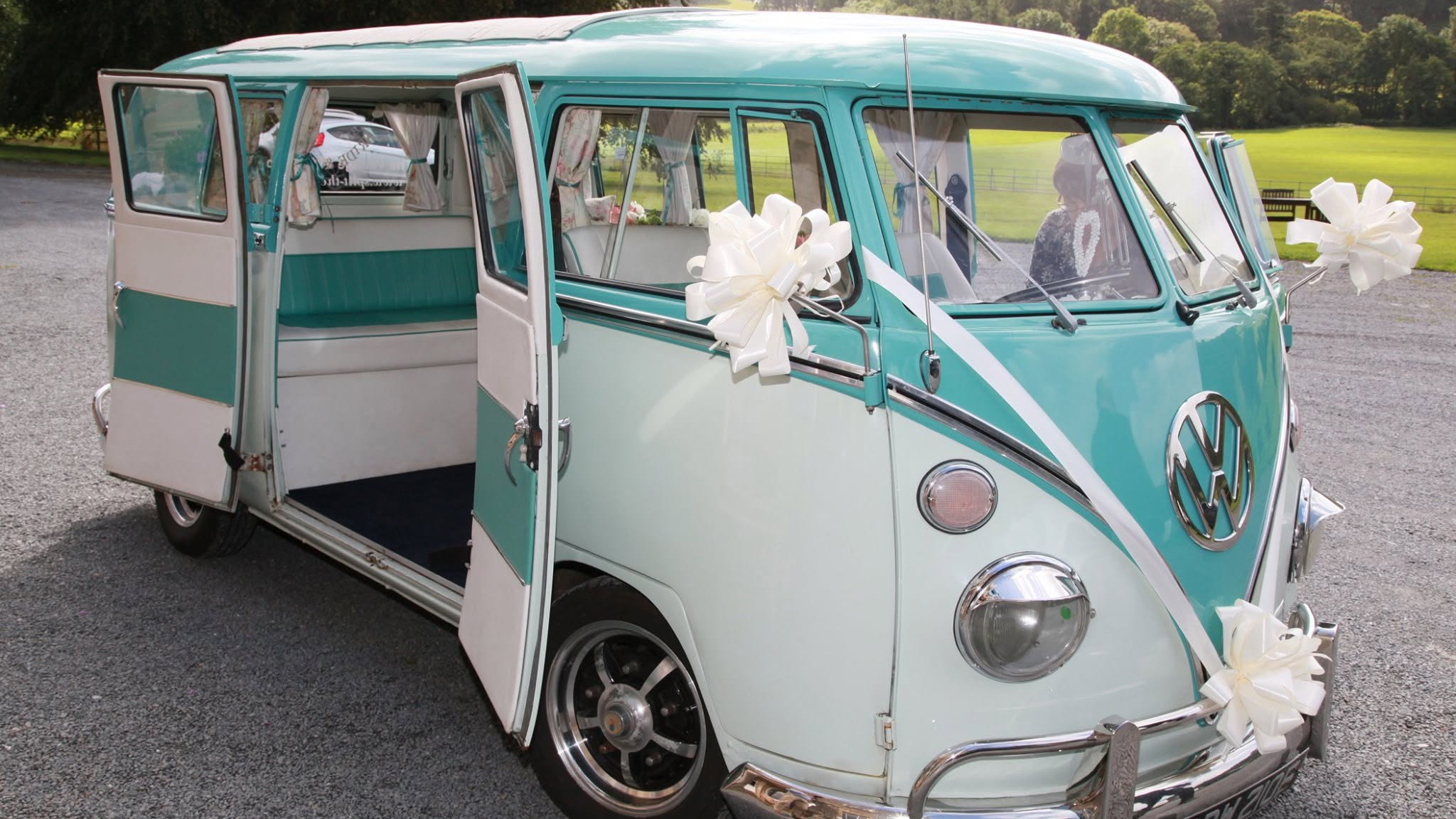 Turquoise and white 1967 Volkswagen Split Screen campervan decorated with large white bows and wedding ribbons.
