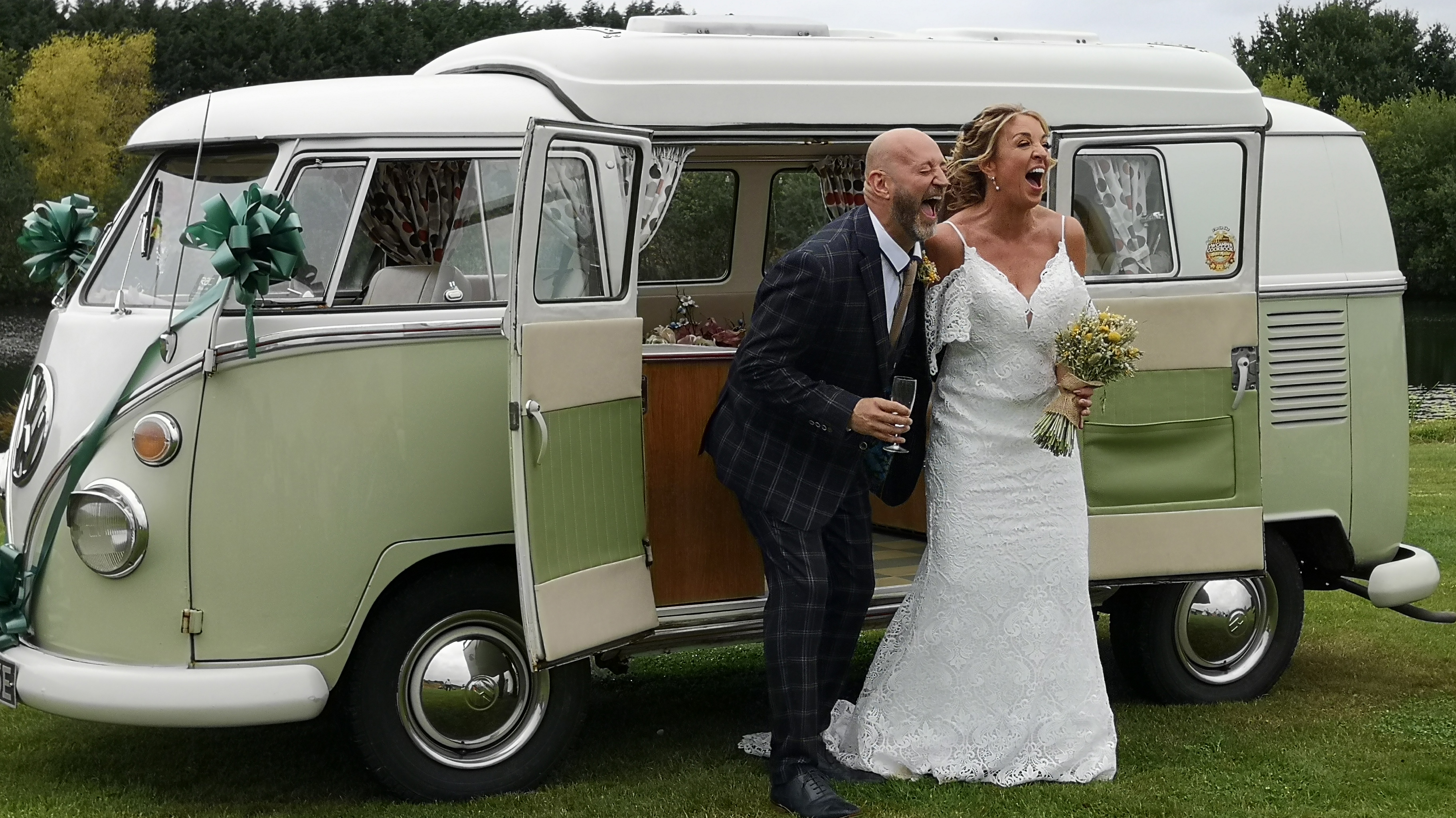 Bride and groom smiling beside cream and green Volkswagen Split Screen campervan on their wedding day.