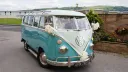 Blue and white 1964 Volkswagen Split Screen Samba campervan with wedding ribbons parked beside the coast.
