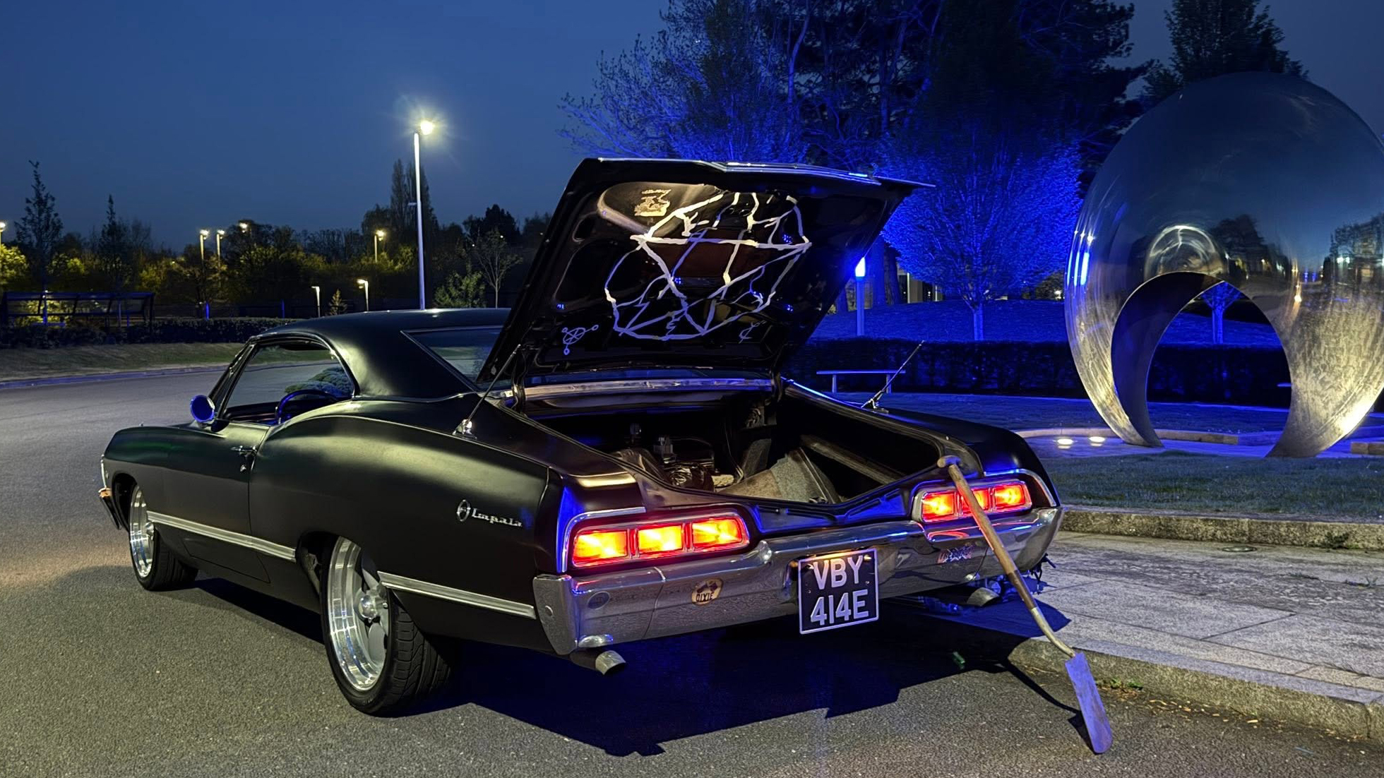 Rear view of black 1967 Chevrolet Impala Fastback with boot open showing Supernatural TV series tribute display.