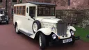 Front three quarter view of Old English White Asquith vintage wedding bus with wooden framed windows and side mounted spare wheel.