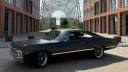 Side view of black 1967 Chevrolet Impala Fastback parked outside modern glass building.