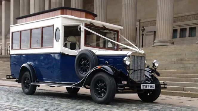 Front three quarter view of navy blue and Old English White Asquith vintage wedding bus with mahogany windows and side mounted spare wheel.