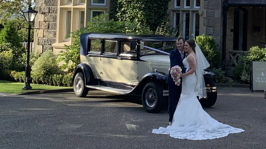 Bride and groom standing beside navy blue and ivory Bramwith Landaulette outside elegant country house wedding venue.