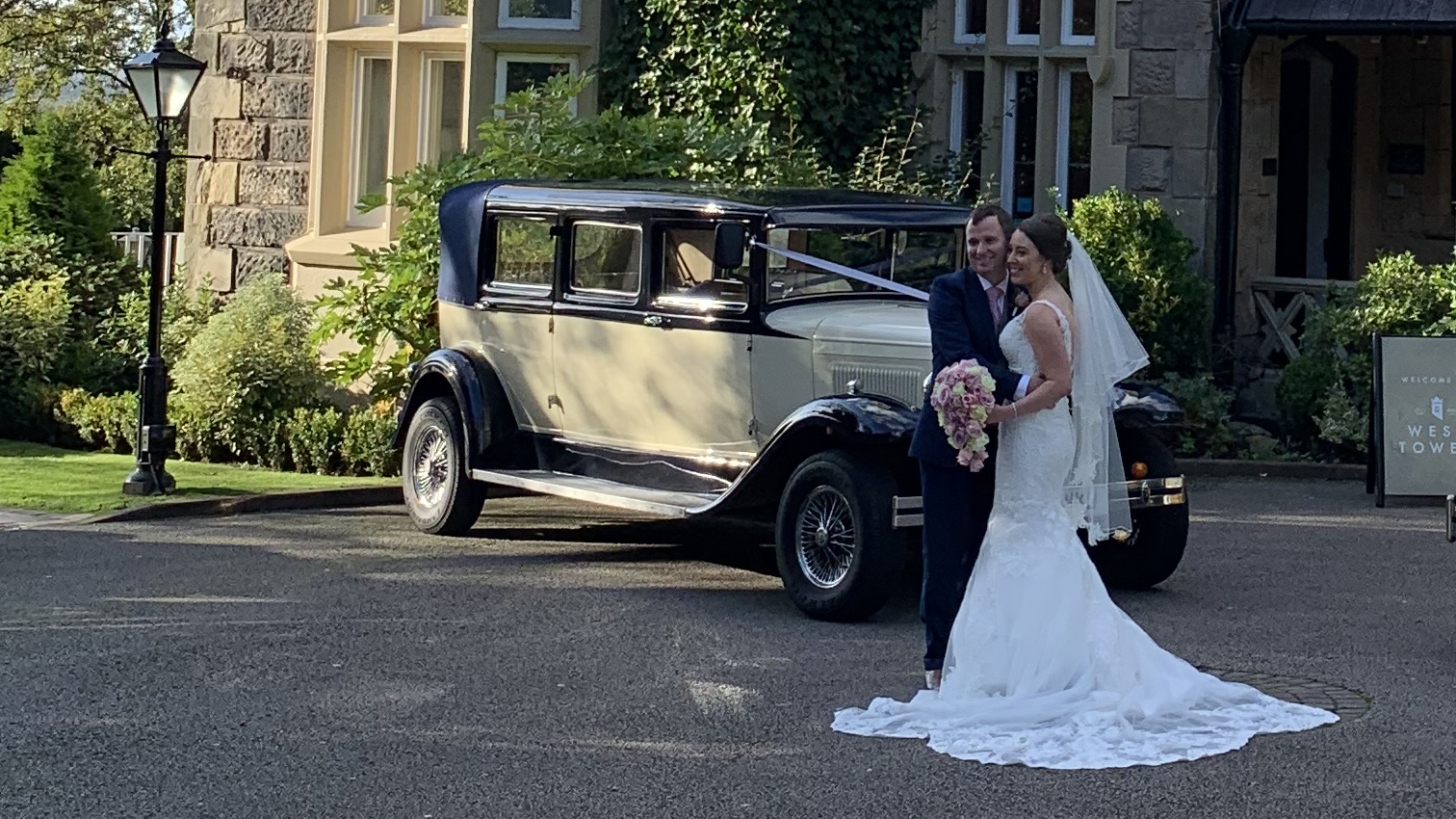 Bride and groom standing beside navy blue and ivory Bramwith Landaulette outside elegant country house wedding venue.