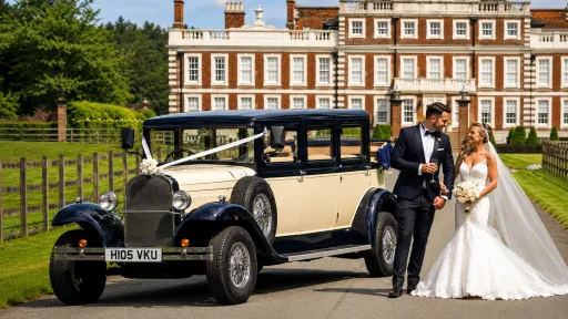 Bride and groom beside navy blue and ivory Bramwith Landaulette decorated with wedding ribbons outside Knowsley Hall near Liverpool.