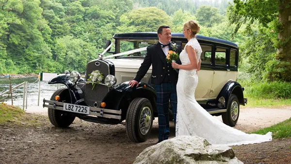 Bride and groom standing beside navy blue and ivory Bramwith limousine at countryside wedding venue.