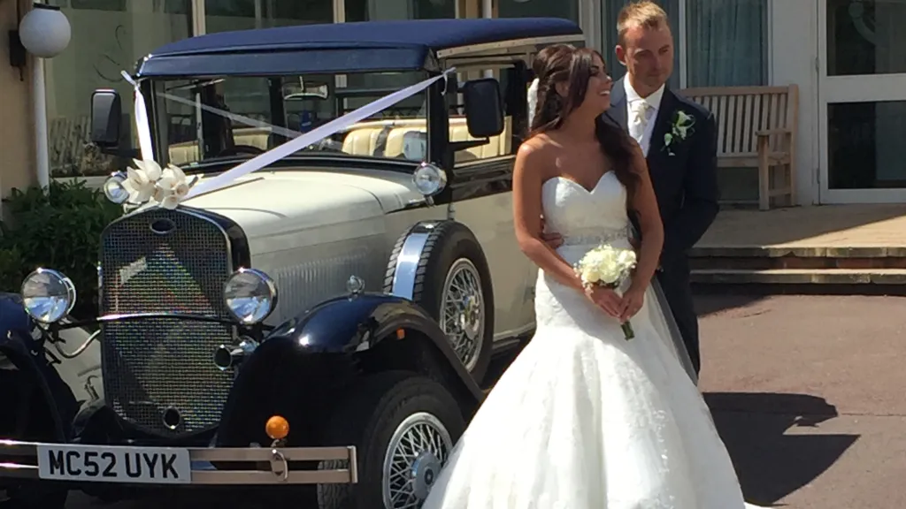 Bride and groom standing beside navy blue and ivory Badsworth Landaulette outside Liverpool wedding venue.