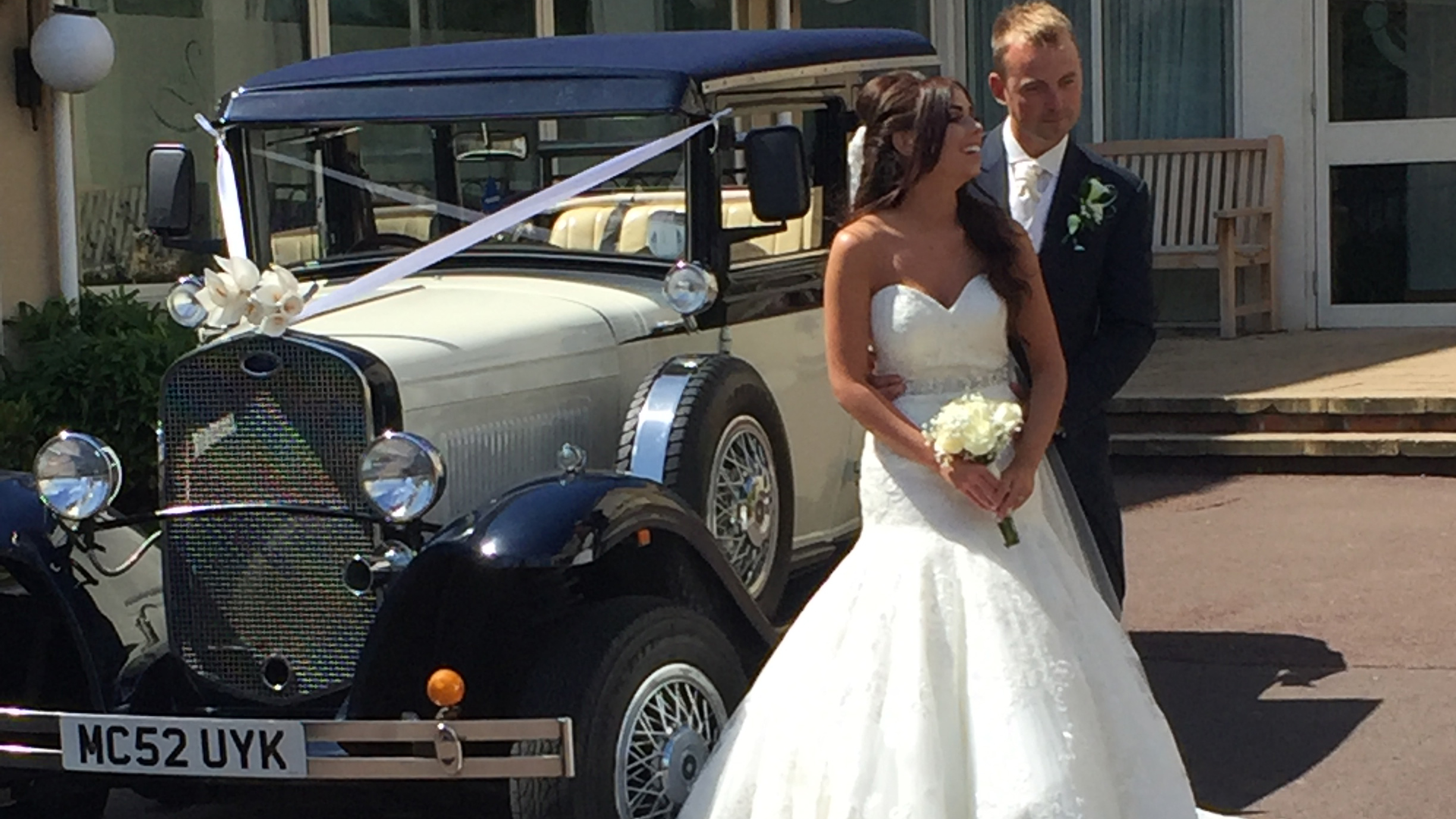 Bride and groom standing beside navy blue and ivory Badsworth Landaulette outside Liverpool wedding venue.