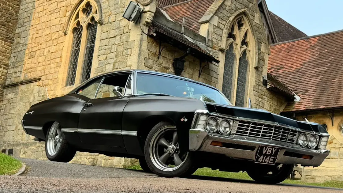 Black 1967 Chevrolet Impala Fastback parked outside historic church showing classic American muscle car styling.