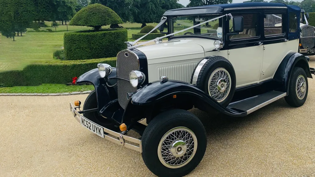 Front three quarter view of navy blue and ivory Badsworth Landaulette with landaulette roof folded back and side mounted spare wheel.