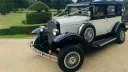Front three quarter view of navy blue and ivory Badsworth Landaulette with landaulette roof folded back and side mounted spare wheel.