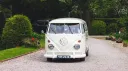 Front view of cream 1972 Volkswagen Split Screen campervan decorated with wedding ribbons entering wedding venue.