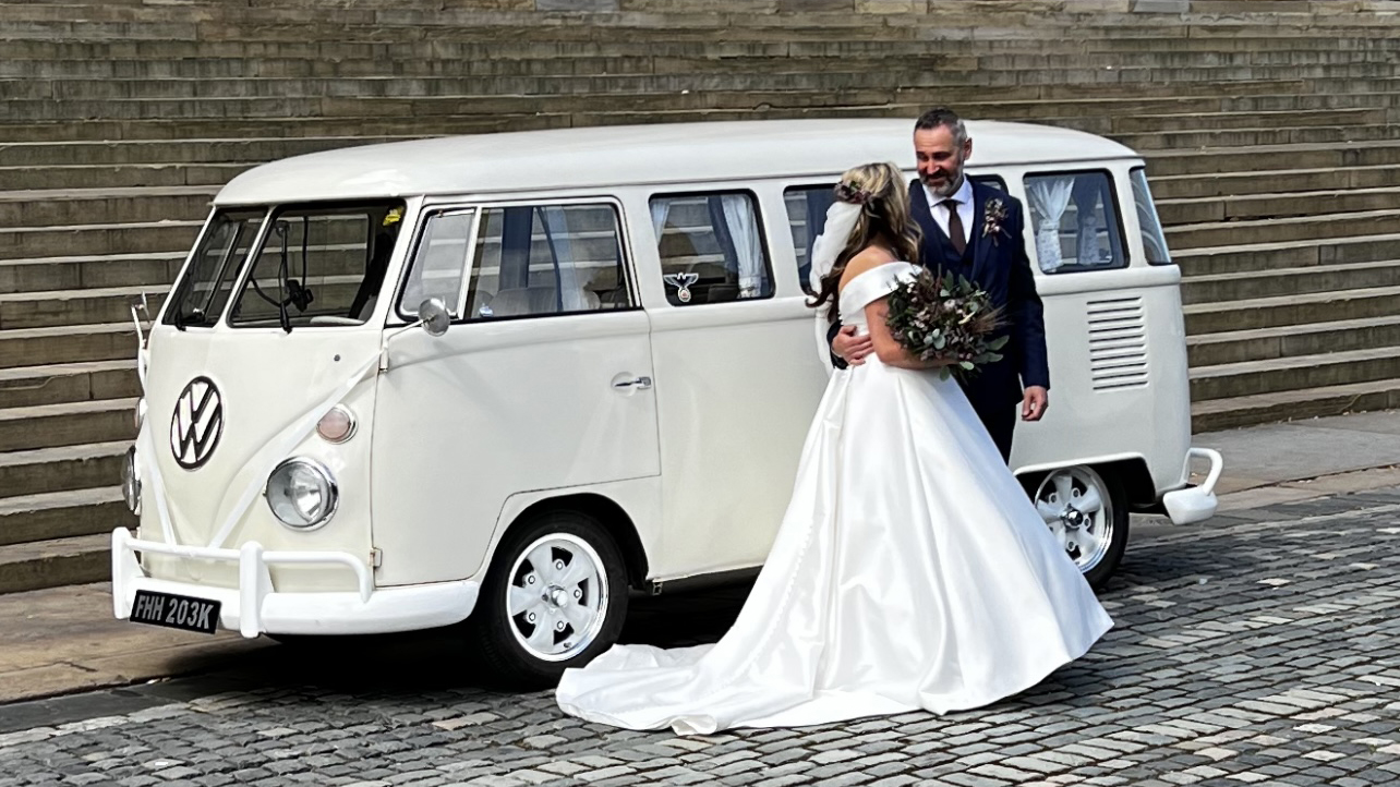 Newly married couple beside cream 1972 Volkswagen Split Screen campervan outside Liverpool Registry Office.