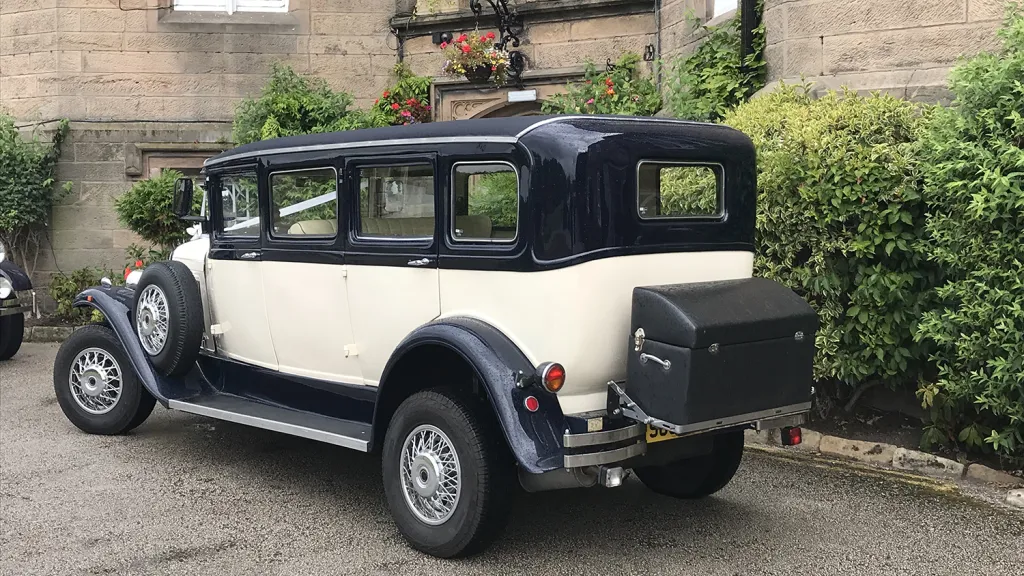 Rear three quarter view of navy blue and ivory Bramwith limousine showing luggage trunk and classic styling.