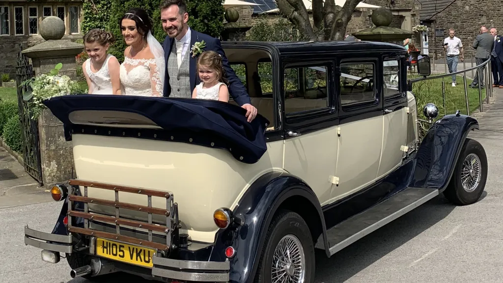 Rear view of navy blue and ivory Bramwith Landaulette with folded rear roof carrying bride, groom and children.