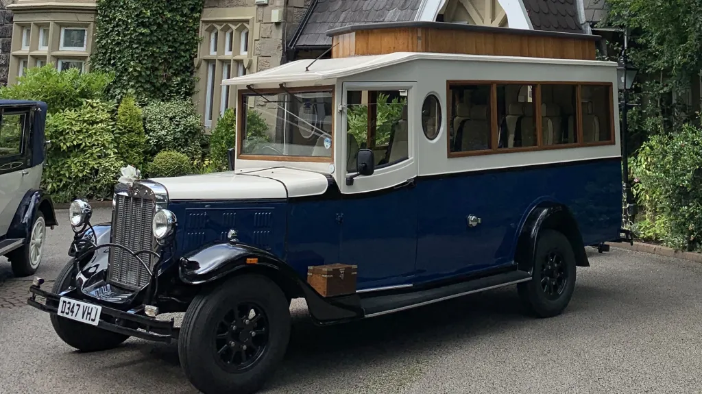 Front three quarter view of navy blue and Old English White Asquith vintage wedding bus outside country wedding venue.