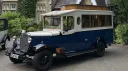 Front three quarter view of navy blue and Old English White Asquith vintage wedding bus outside country wedding venue.