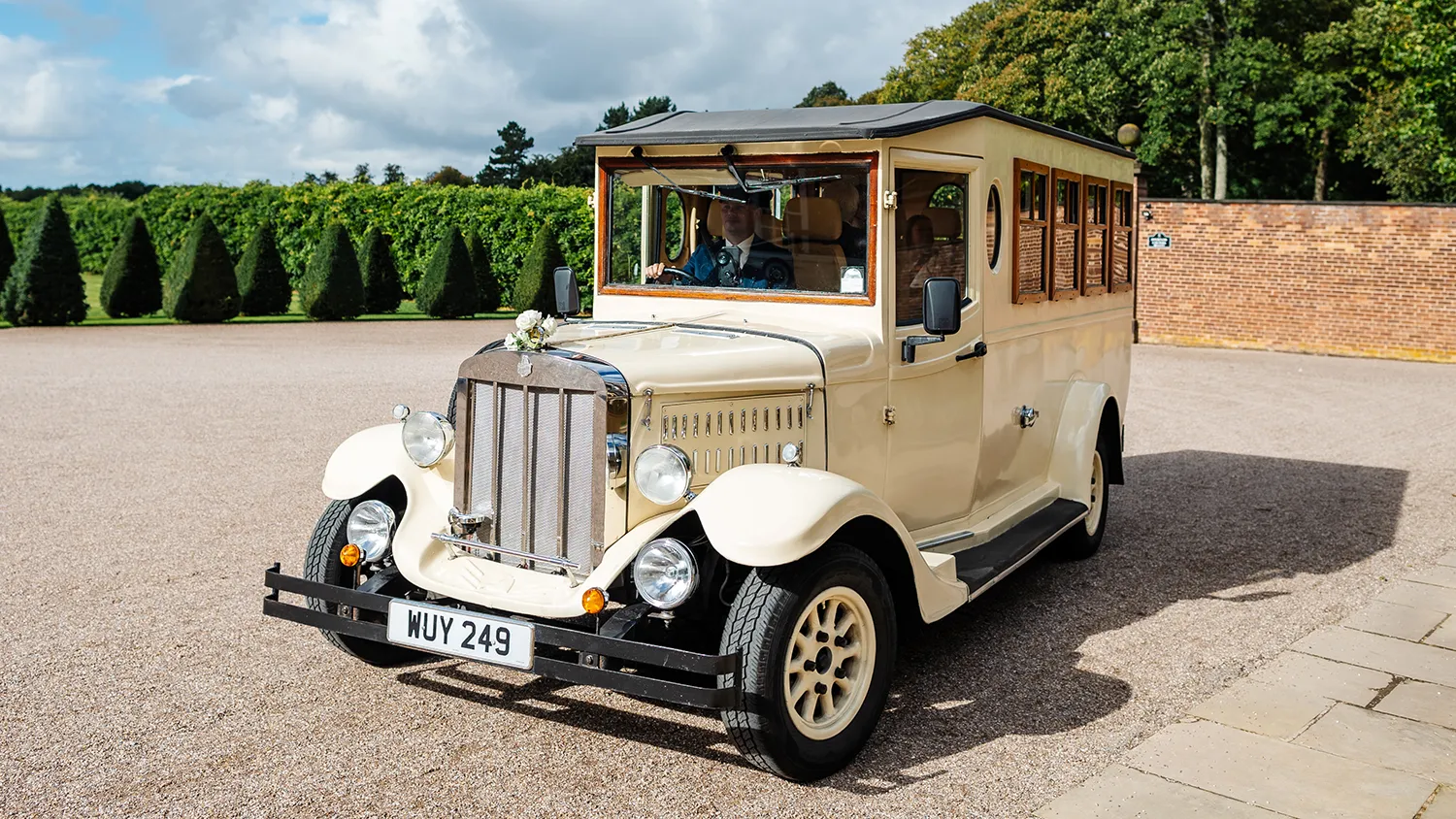Front three quarter view of Old English White Asquith vintage wedding bus parked outside wedding venue courtyard.