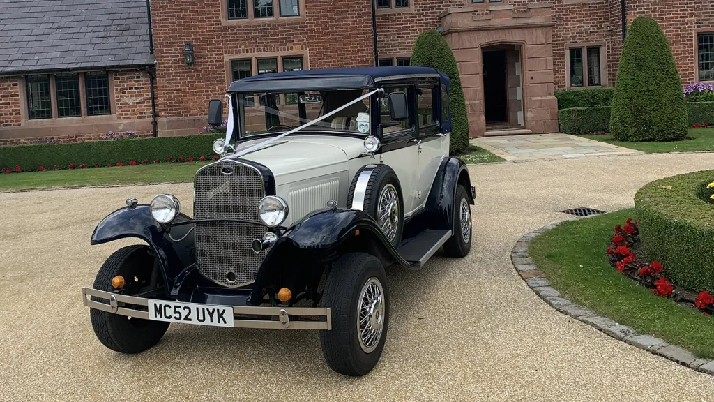 Navy blue and ivory Badsworth Landaulette parked outside country house with chrome headlamps and wire wheels.