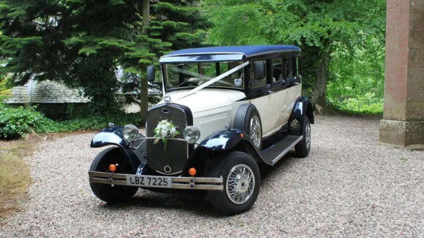 Front three quarter view of navy blue and ivory Bramwith limousine parked outside historic wedding venue.