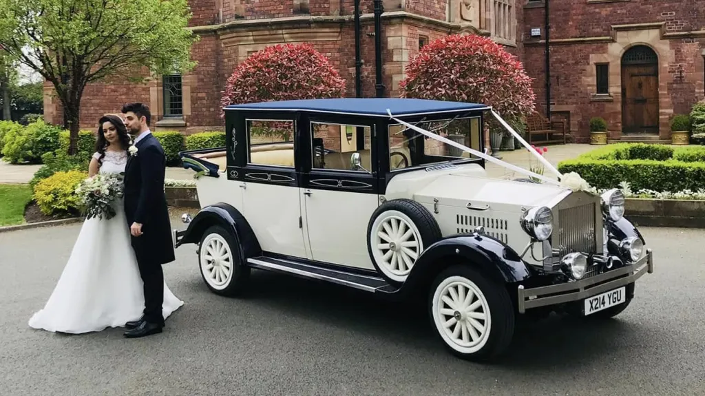 Bride and groom standing beside ivory and navy blue Imperial Landaulette outside Liverpool wedding venue.