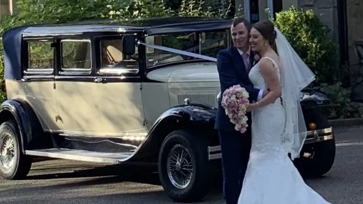 Bride and groom beside navy blue and ivory Bramwith Landaulette decorated with white wedding ribbons.